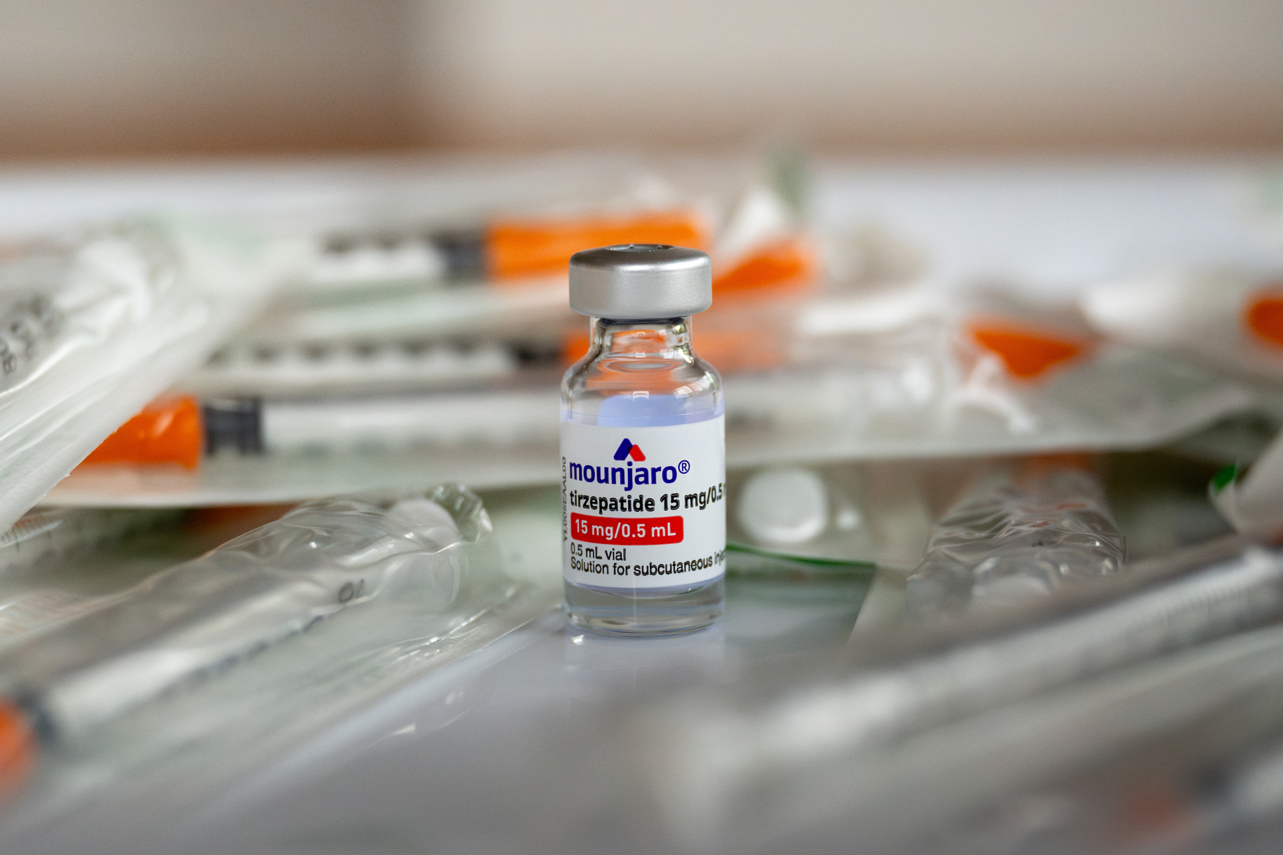 A medical vial of Mounjaro (tirzepatide) 15 mg/0.5 mL solution sits among medical syringes and supplies on a white surface, showing the injectable diabetes medication used for subcutaneous administration.