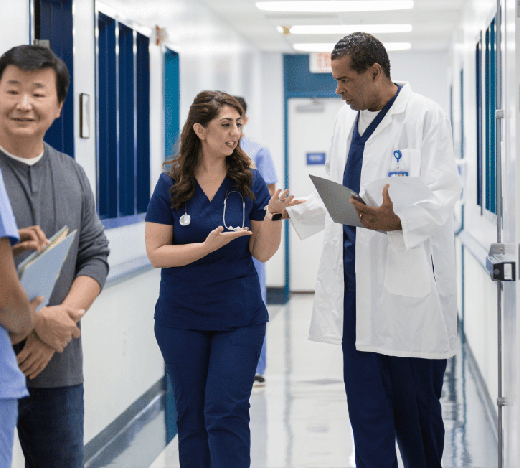 Healthcare professionals including a doctor in a white coat and nurses in blue scrubs have a discussion in a modern hospital hallway with blue and white interior design.
