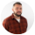 A person wearing a dark red or maroon colored top against a neutral background, shown from approximately chest up in a portrait-style photo.