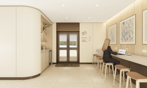 A modern office lobby or waiting area with light wood finishes features a curved reception desk, high-top seating along a wall counter where a woman works on a laptop, directional signage, and glass doors leading to other areas.