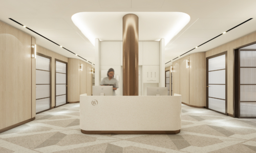 A modern, luxurious lobby features a curved white reception desk with a distinctive bronze cylindrical column, surrounded by elevator banks with frosted glass doors and warm beige finishes throughout the space.