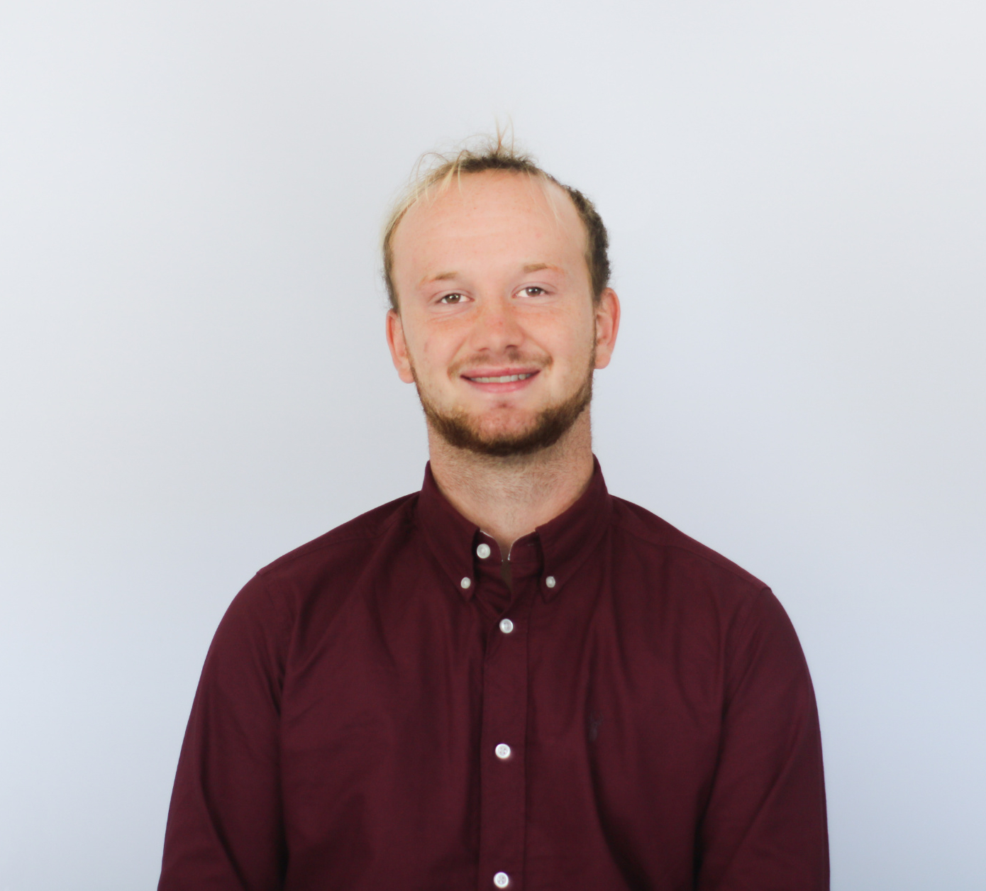 A smiling man with blonde hair and a beard wearing a burgundy button-down shirt against a white background in what appears to be a professional headshot photo.