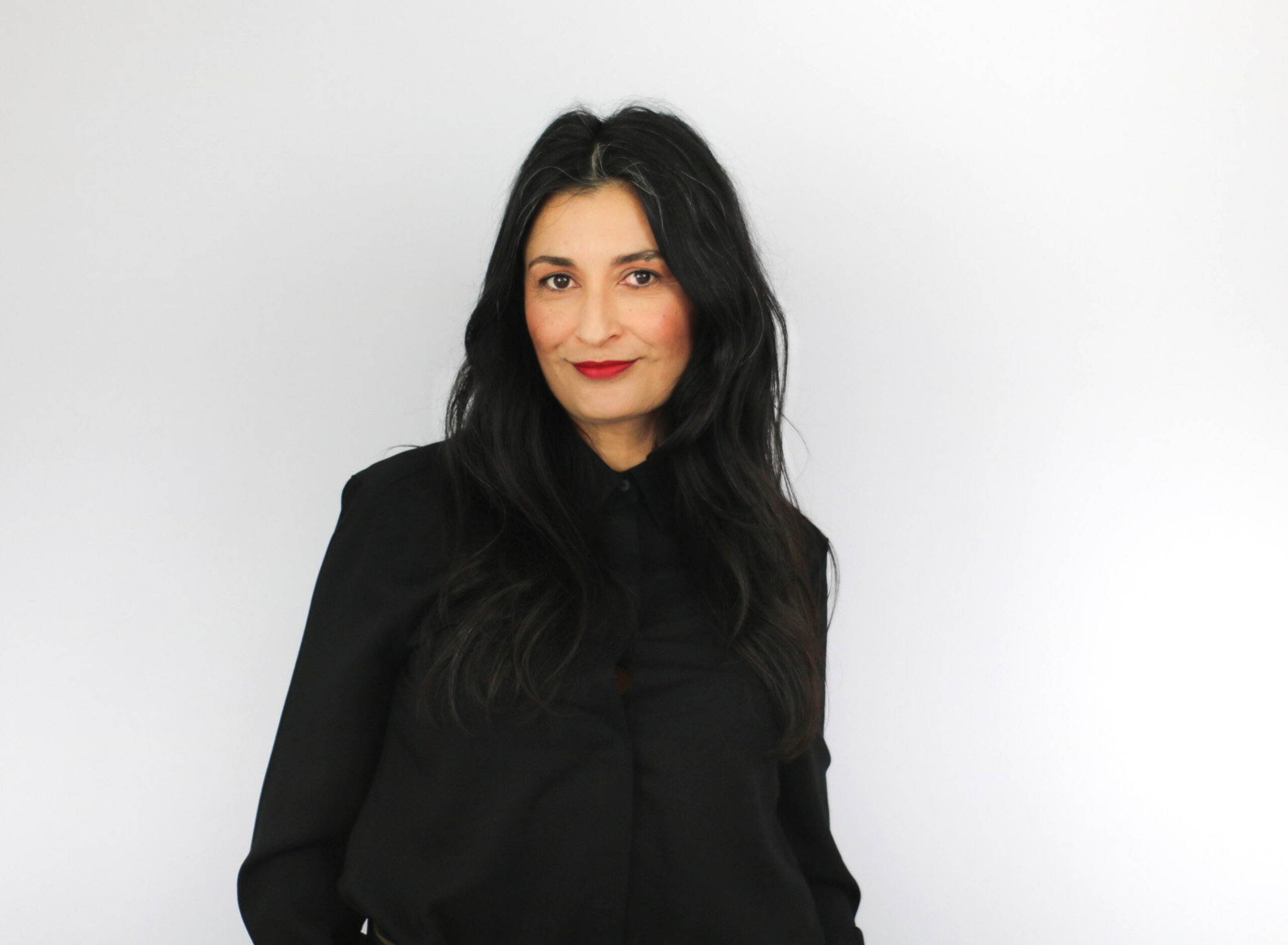 A woman with long dark hair wearing a black hoodie smiles at the camera against a white background, appearing to be in a professional headshot or portrait setting.